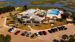 An aerial view of a resort with a swimming pool, water slides, and a parking lot. - Affordable Lodging for Business and Leisure Travelers l Kitchen & Pool (Ingleside)