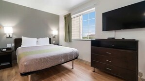 A bedroom with a bed, bedside lamps, a dresser, a TV, and a window with curtains. - Affordable Lodging for Business and Leisure Travelers l Kitchen & Pool (Ingleside)