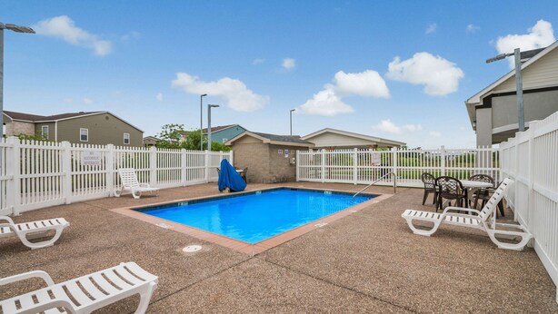 A swimming pool with lounge chairs and a fence, surrounded by buildings. - Affordable Lodging for Business and Leisure Travelers l Kitchen & Pool (Ingleside)