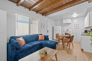 Un espacio habitable compacto con un sofá azul, una mesa de comedor de madera y una zona de cocina.