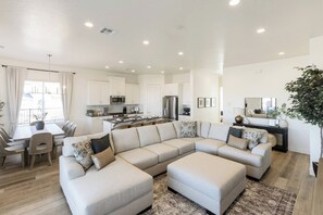 A modern living room with a sectional sofa, a dining area, and a kitchen.