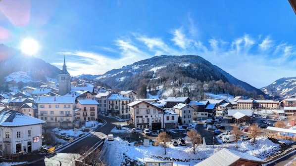 Eine verschneite Stadt mit einem markanten Kirchturm, einem zentralen Platz mit Gebäuden und einer Bergkulisse im Hintergrund.