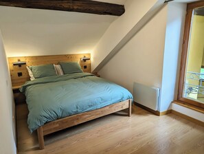 Ein Schlafzimmer mit schrägem Dach, einem Holzkopfteil und einem Bett mit grüner Bettwäsche.
