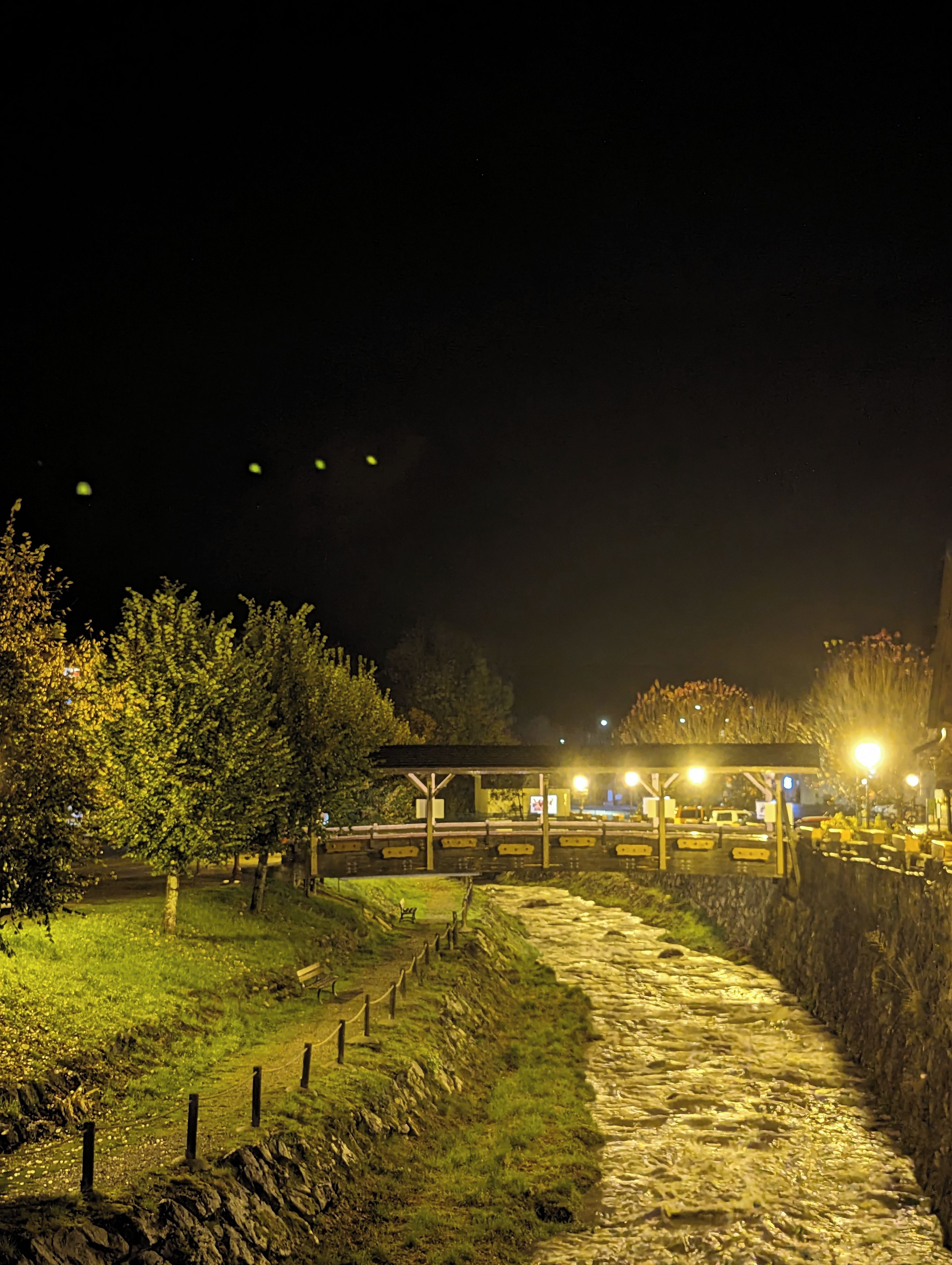 Escena nocturna con un sendero pavimentado que conduce a una zona cubierta con bancos.