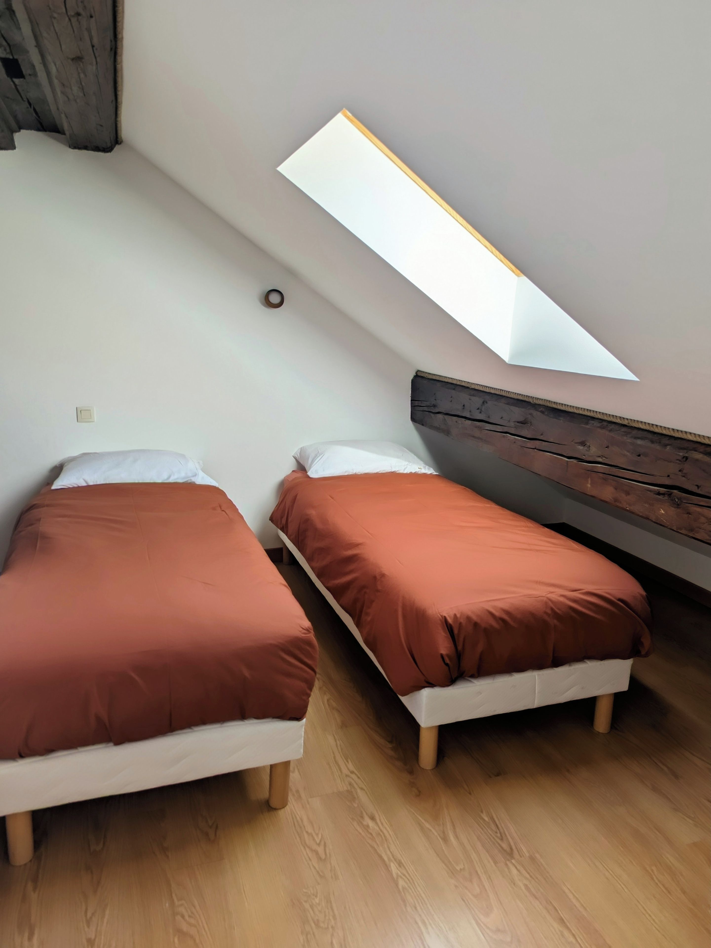 A room with two beds, a skylight, wooden flooring, and a sloped ceiling.