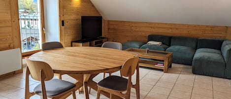 A cozy living room with a wooden dining table, chairs, a green sofa, and a television.