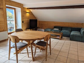 A cozy living room with a wooden dining table, chairs, a green sofa, and a television. - 100m² Duplex with mountain views, in the heart of Beaufort (Beaufort)