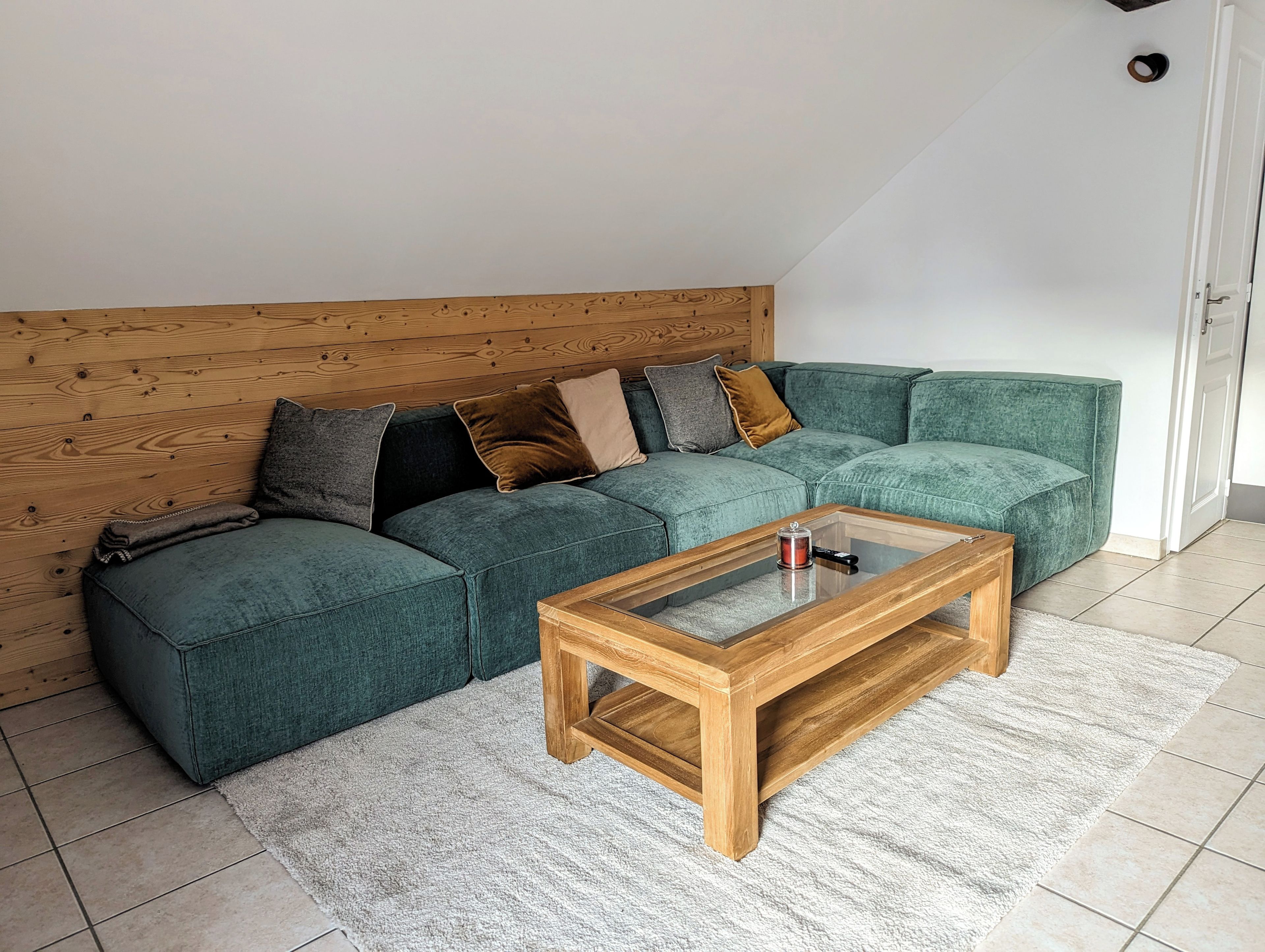Uma sala de estar moderna com um sofá seccional verde, uma mesa de centro de madeira e um tapete branco.