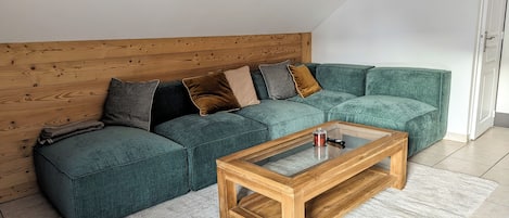 A modern living room with a green sectional sofa, a wooden coffee table, and a white carpet.