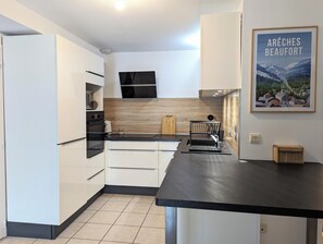 A modern kitchen with white cabinetry, a black countertop, and a wooden backsplash. - 100m² Duplex with mountain views, in the heart of Beaufort (Beaufort)