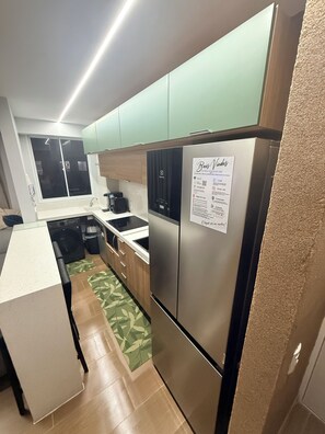 Una cocina moderna con electrodomésticos de acero inoxidable, horno empotrado y refrigerador. Hay una ventana con vistas al exterior y un tapete de piso con diseño verde.