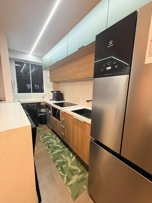 A modern kitchen with stainless steel appliances, wooden cabinets, and a green patterned rug. - Modern Apartment with Ocean View, Praia do Futuro | Air Conditioning and Parking Space. (Fortaleza)