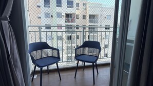 A balcony with two chairs, a view of a building with balconies, and a curtain partially covering the window. - Modern Apartment with Ocean View, Praia do Futuro | Air Conditioning and Parking Space. (Fortaleza)