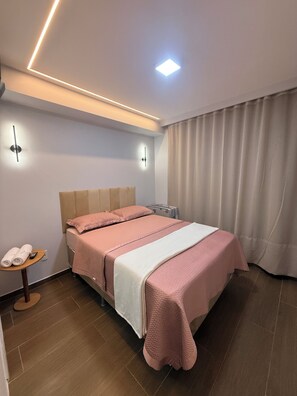Une chambre d’hôtel moderne, équipée d’un lit, d’une table de chevet avec une télécommande et d’un luminaire fixé au mur.