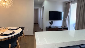 A modern interior with a dining area, a kitchen island, a flat-screen TV, and a ceiling light fixture. - Modern Apartment with Ocean View, Praia do Futuro | Air Conditioning and Parking Space. (Fortaleza)
