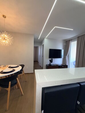 Ein modernes Interieur mit Essbereich, Kücheninsel, Flachbildfernseher und Deckenleuchte.