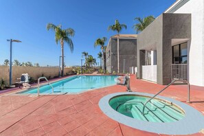 Ein Schwimmbecken mit Whirlpool, umgeben von Palmen und einem Gebäude mit einem Ziegeldach.