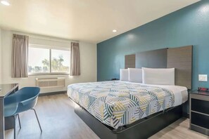 Ein Hotelzimmer mit Bett, Schreibtisch, Stuhl, einem Fenster mit Vorhängen und einem Nachttisch mit einer Uhr.