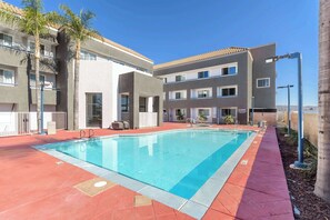 Ein Swimmingpool mit einer roten und blauen Fliesenverkleidung, umgeben von einem mehrstöckigen Gebäude mit Balkonen und Fenstern.