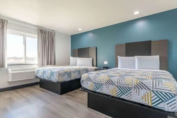 Ein Hotelzimmer mit zwei Betten, einem Fenster mit Vorhängen und einer blauen Akzentwand.