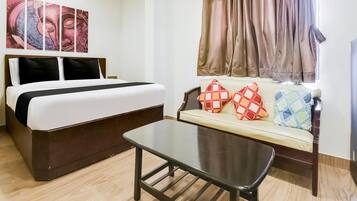 A hotel room with a bed, a sofa with patterned cushions, a coffee table, and a window with curtains.