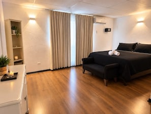 Habitación de hotel con cama, sofá, una mesita con una planta y aire acondicionado instalado en la pared.