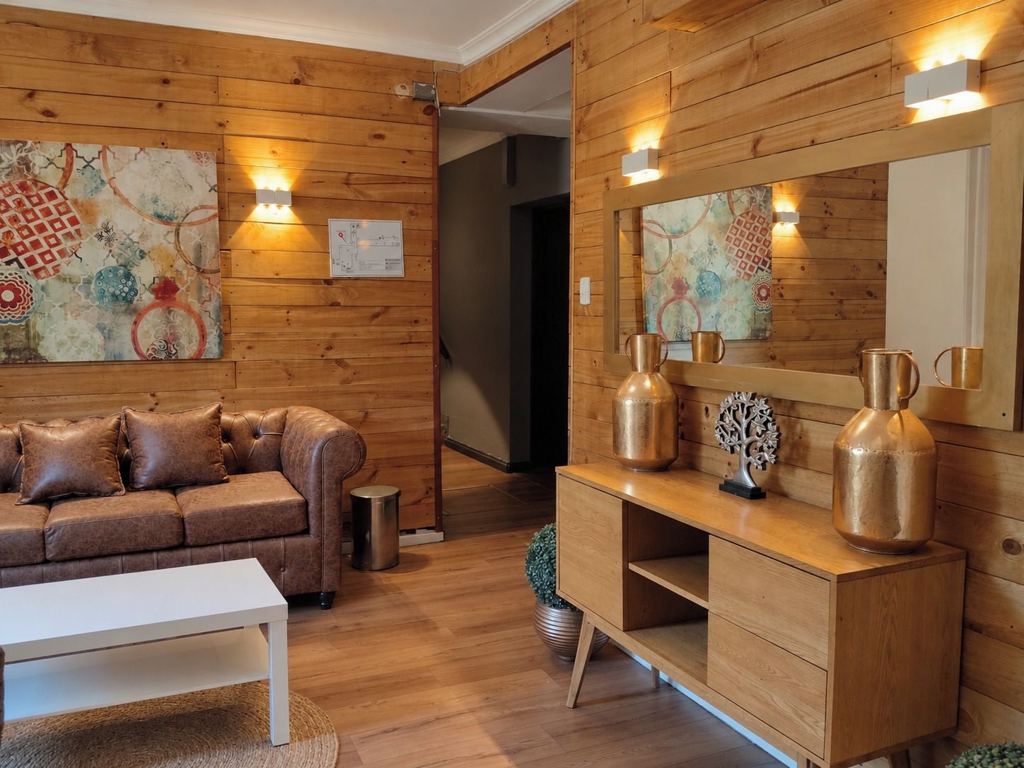 Una habitación con paredes de madera, un sofá de cuero marrón, una mesa de centro blanca y un mueble de madera con adornos.