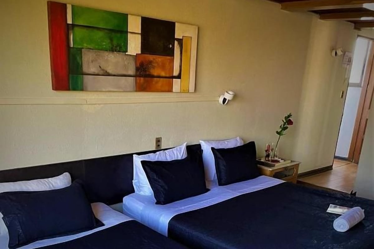 A hotel room with two beds, a painting on the wall, and a small table with a vase.