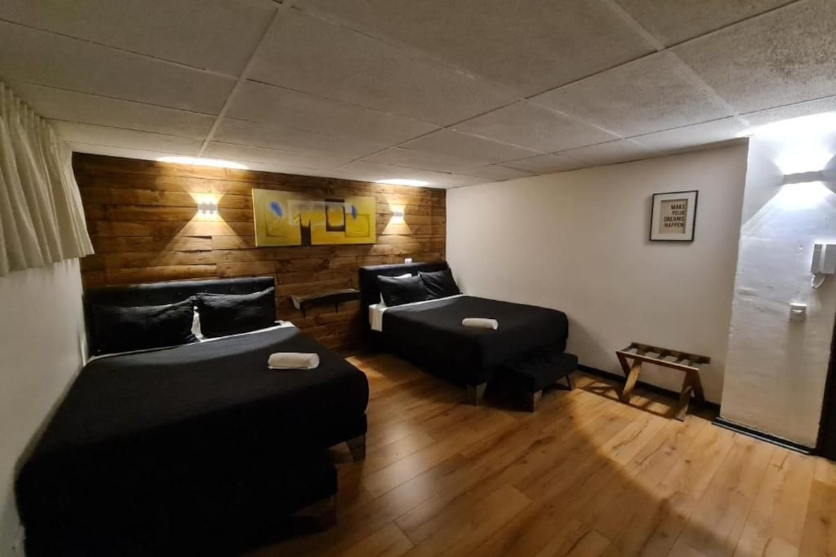 A room with two beds, wooden flooring, a wall-mounted light fixture, and a framed picture.