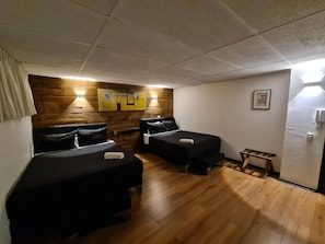 Una habitación con dos camas, suelo de madera, una lámpara de pared e imagen enmarcada.