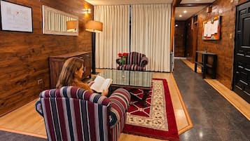 A room with a wooden wall, a striped sofa, a glass coffee table, and a red rug.
