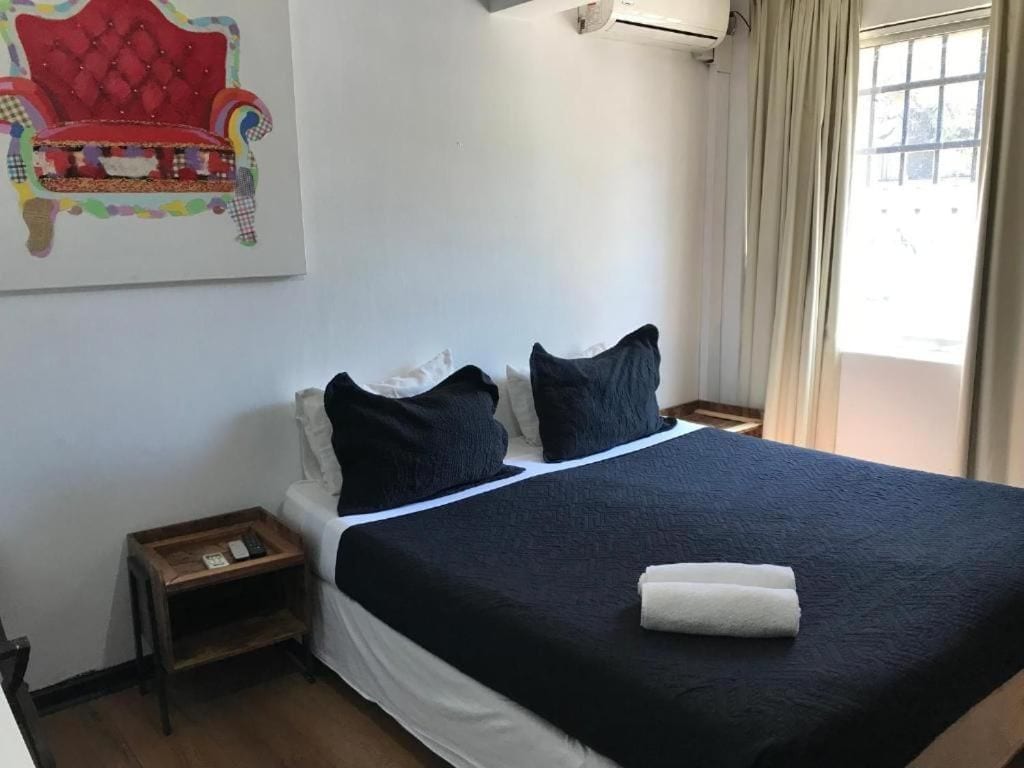 Una habitación de hotel con cama, mesita de noche, aire acondicionado instalado en la pared y una ventana con cortinas.