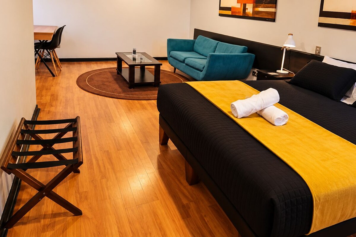 A hotel room with a bed, a sofa, a small table, and a chair.