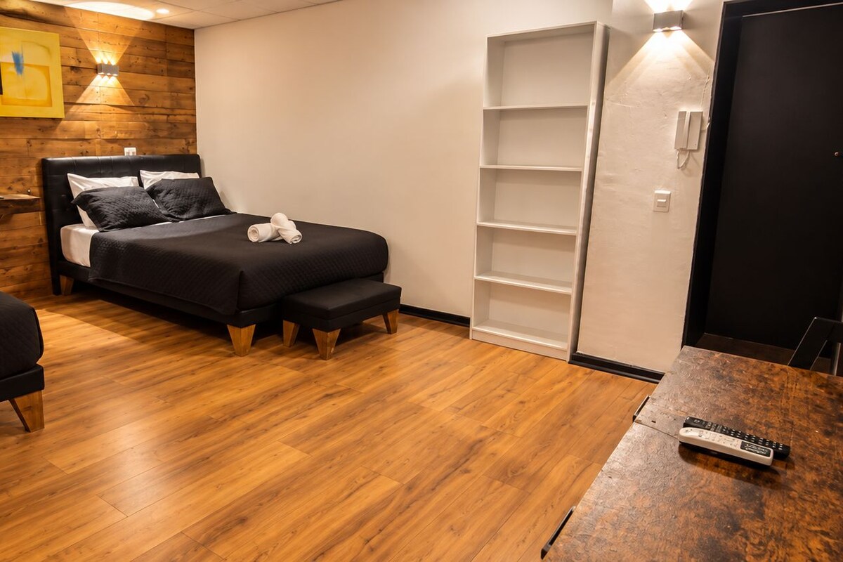 A hotel room with two beds, wooden flooring, a desk with a remote control, and a wardrobe.