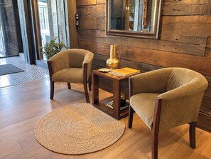 A room with two armchairs, a small wooden table, a woven rug, and a wooden wall with a mirror.