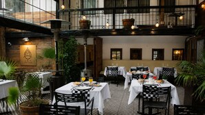 An indoor dining area with checkered flooring, tables set with white tablecloths, and black chairs. - LRH Santiago (Santiago)