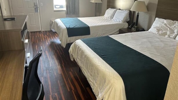Quarto de hotel com duas camas, uma escrivaninha, uma cadeira e uma janela com cortinas.