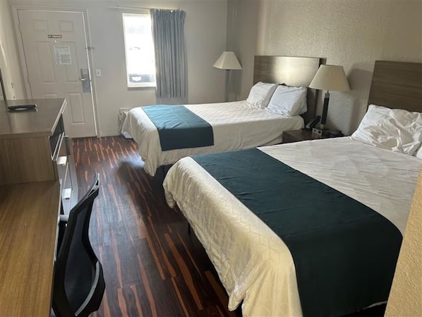 Habitació d'hotel amb dos llits, un escriptori, una cadira i una finestra amb cortines.