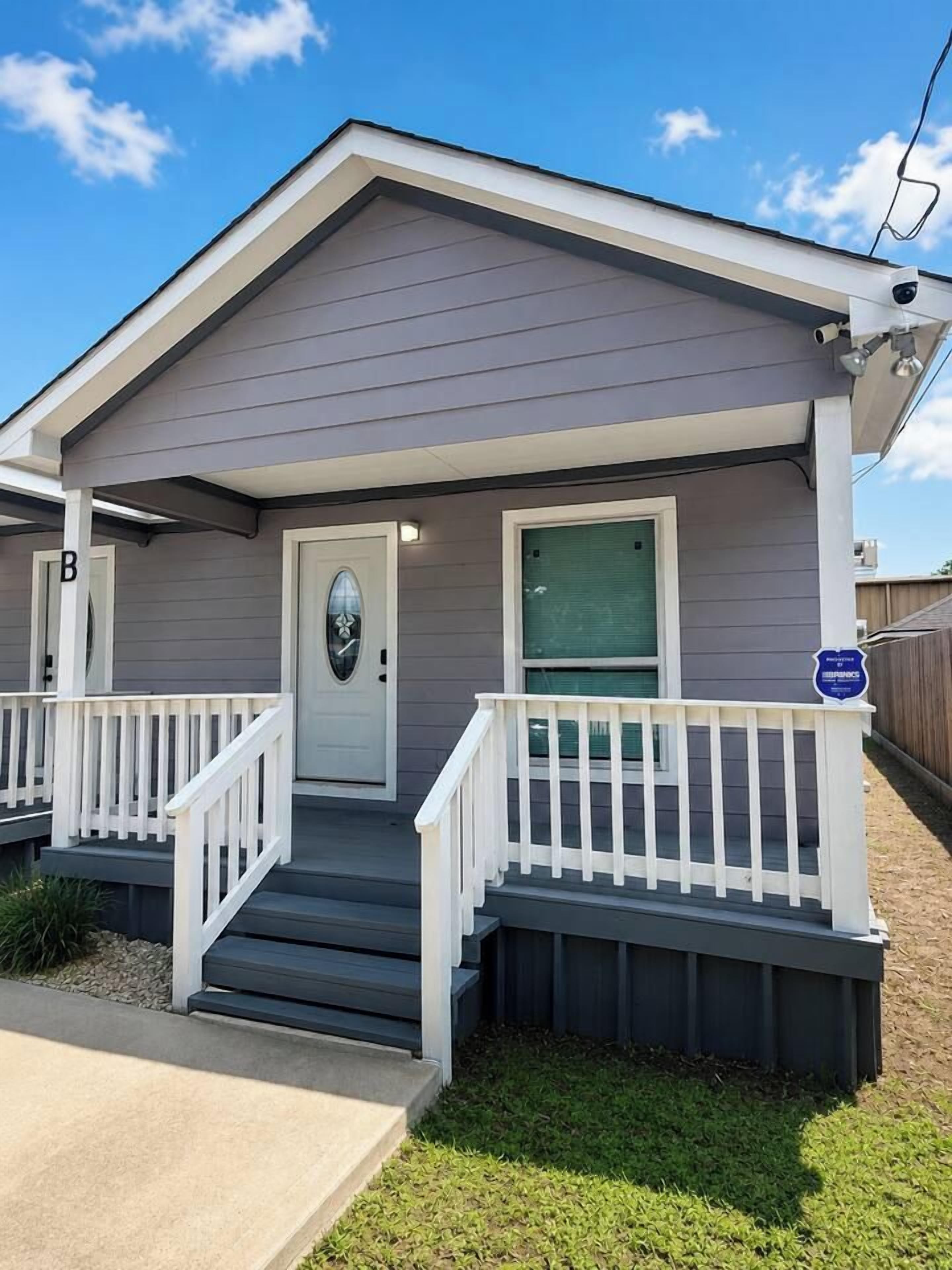 A two-story residential building with a front porch, a door with a glass panel, and a mailbox.