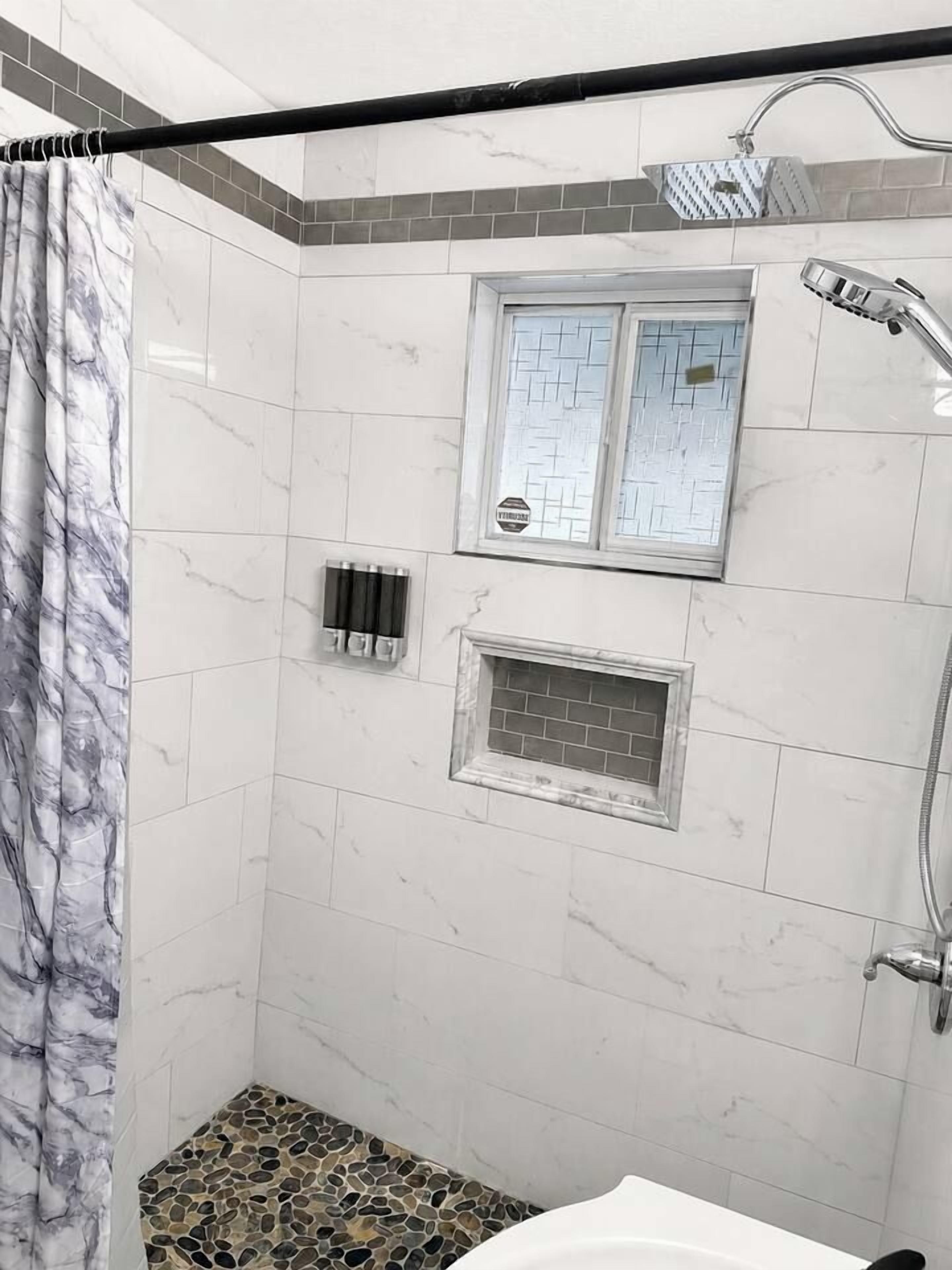 Ein Badezimmer mit Dusche, Fenster und gefliestem Boden.