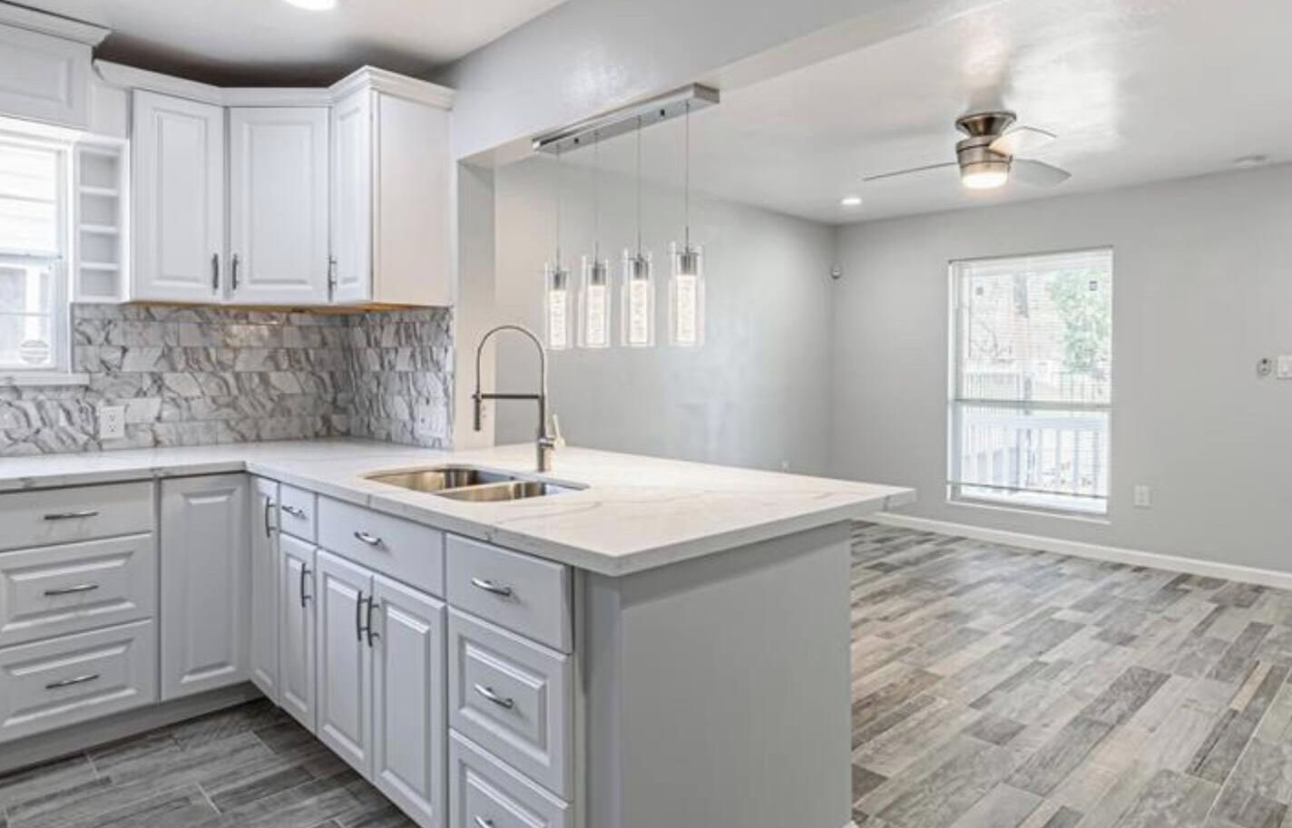 A modern kitchen with white cabinetry, a marble backsplash, and a large island with a sink.