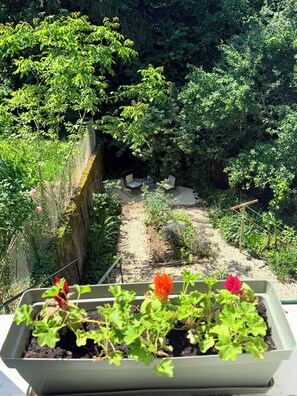 Un jardin avec un chemin de gravier, un espace aménagé avec des chaises et une clôture en métal.
