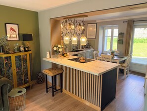 Une cuisine moderne dotée d’un îlot central, de lambris en bois, de luminaires suspendus et offrant une vue sur l’extérieur.