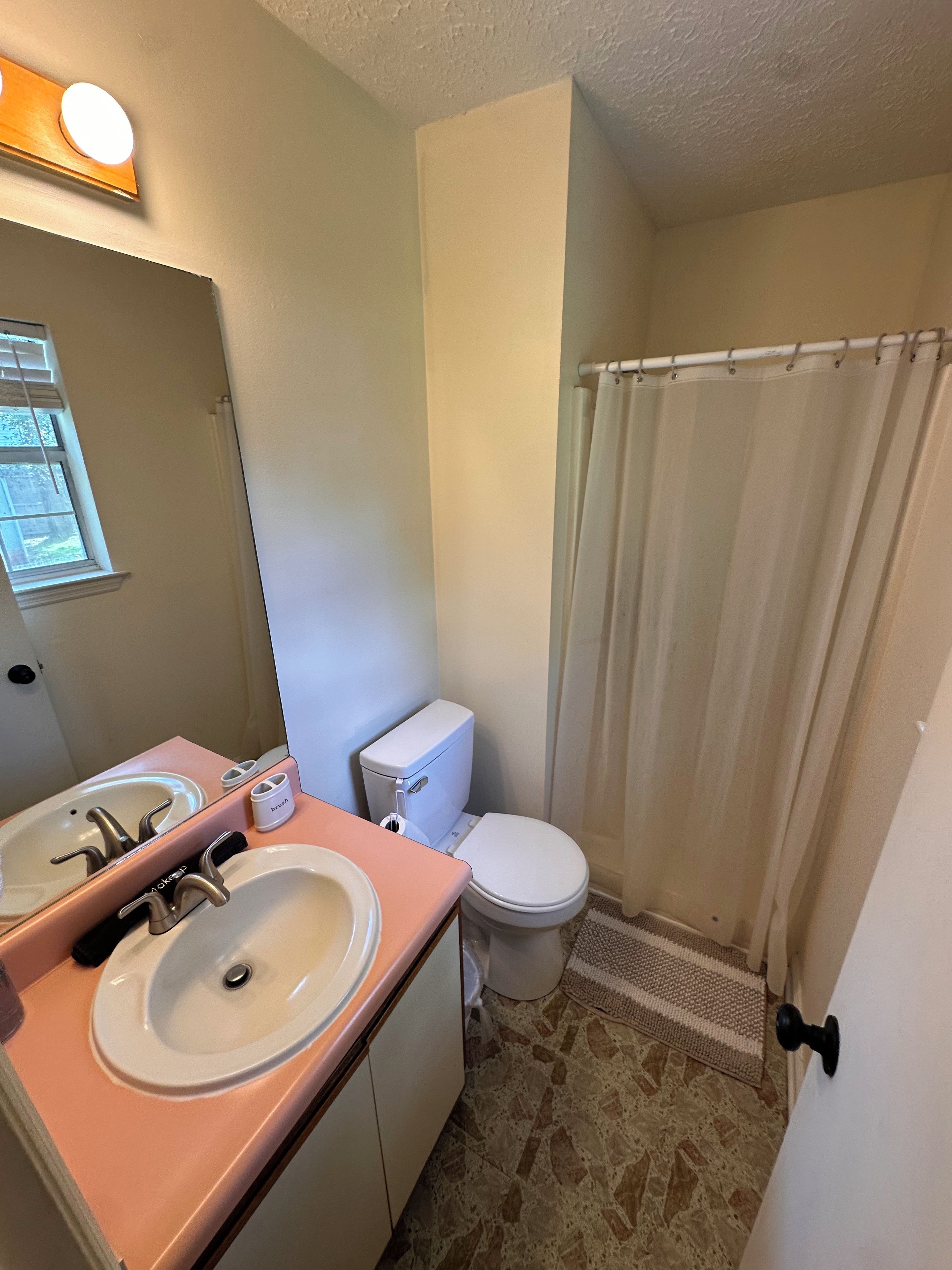Un baño con inodoro, dos lavamanos, espejo y cortina de ducha.