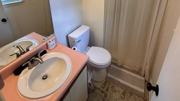 Un baño con inodoro, dos lavamanos, espejo y cortina de ducha.