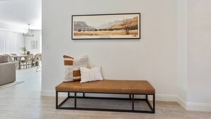 A modern living room with a bench, a framed landscape painting, and a dining area in the background. - 3 Master Suites with Private Baths, Kings Beds, Private Hot Tub, EV, BBQ (Washington)
