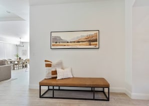 A modern living room with a bench, a framed landscape painting, and a dining area in the background. - 3 Master Suites with Private Baths, Kings Beds, Private Hot Tub, EV, BBQ (Washington)