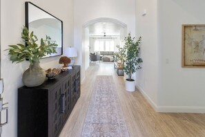 A hallway with a dark wooden console, a mirror, a vase with green plants, a white potted tree, and a framed map on the wall.