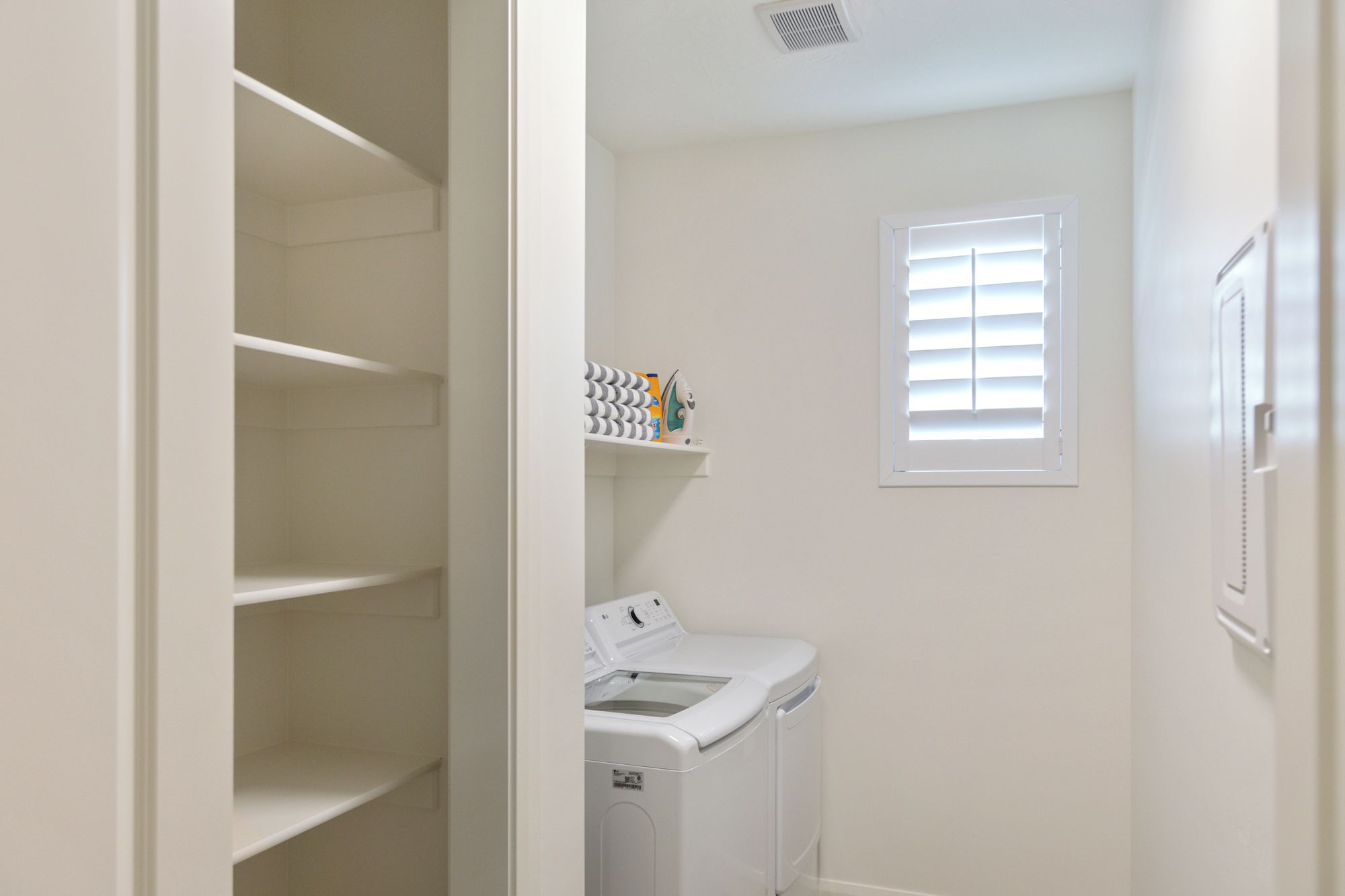A laundry room with a washing machine, a dryer, and a shelf with laundry supplies.