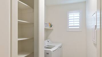 A laundry room with a washing machine, a dryer, and a shelf with laundry supplies.